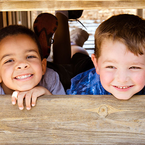 Two smiling children looking over a wooden play structure